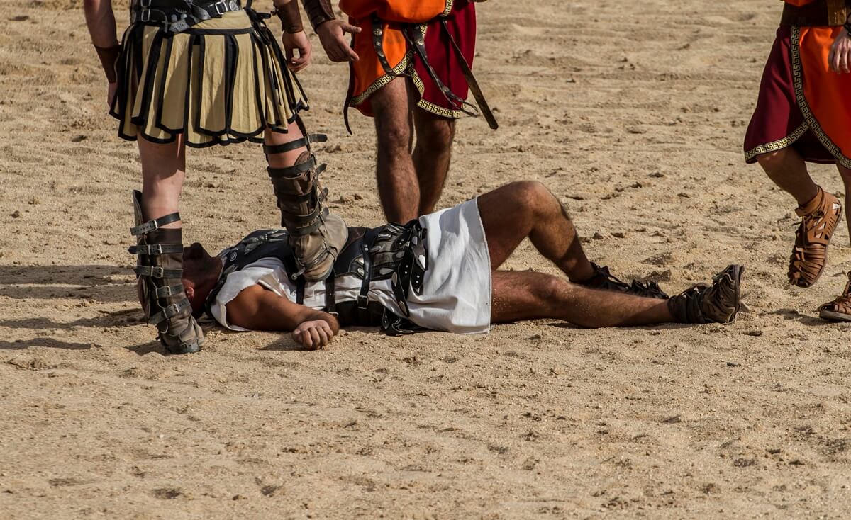 A fallen Roman gladiator lying on the sandy floor of the arena